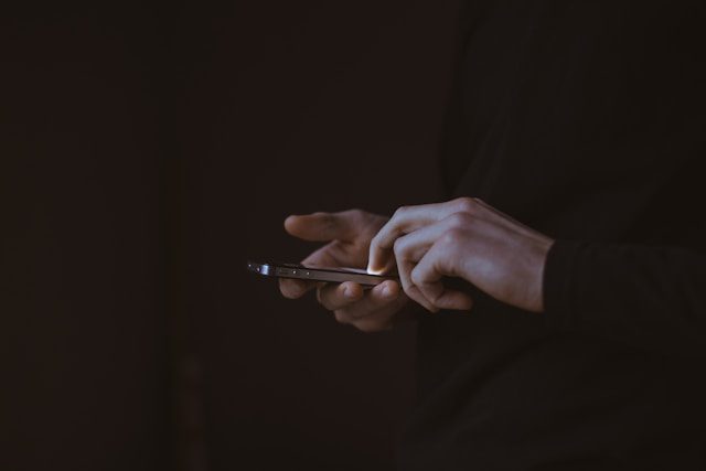 A person using a smartphone in low light, symbolizing the quiet disappearance of identity in the age of the digital afterlives.