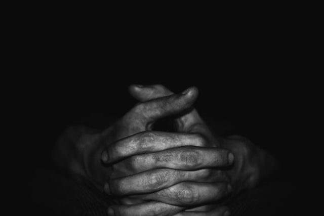 Black-and-white photo of clasped hands in shadow, symbolizing intergenerational silence and the emotional weight of diaspora trauma inheritance.